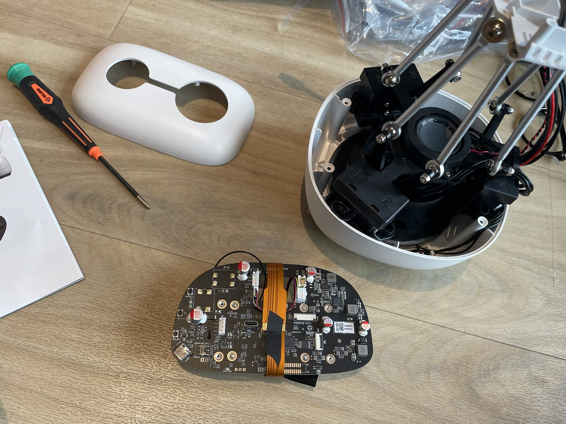 A partially assembled Reachy Mini robot with its circuit board, shell, tools, and internal mechanism visible